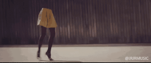 a woman in a yellow skirt and black tights is dancing in front of a wall .