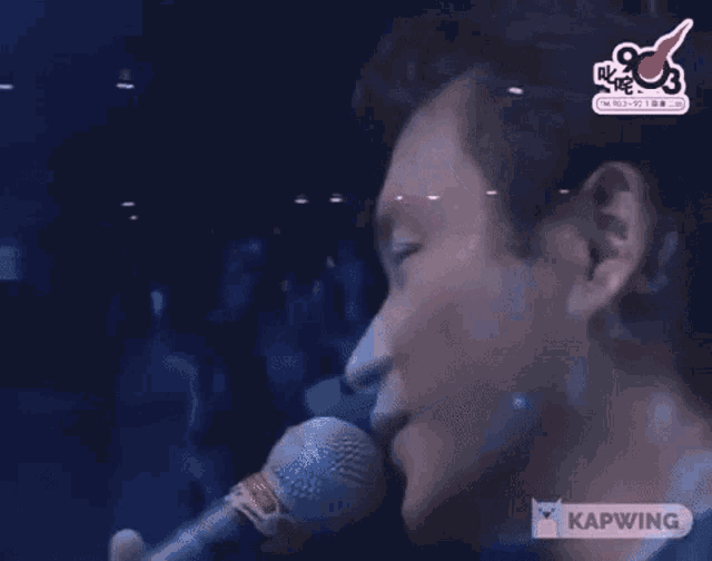 a man in a suit is singing into a microphone and covering his face with his hands .