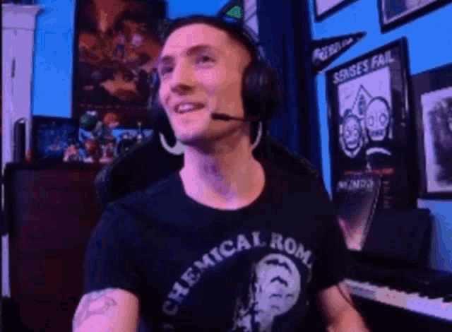 a man wearing headphones and a shirt that says `` chemical rom '' is sitting in front of a piano .
