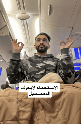 a man in a camo sweatshirt is sitting on a plane