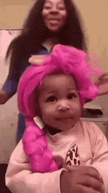 a little girl is wearing a pink wig while a woman holds her .