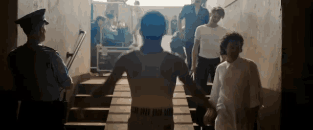 a man with a tattoo on his back is walking down stairs with a police officer standing behind him .