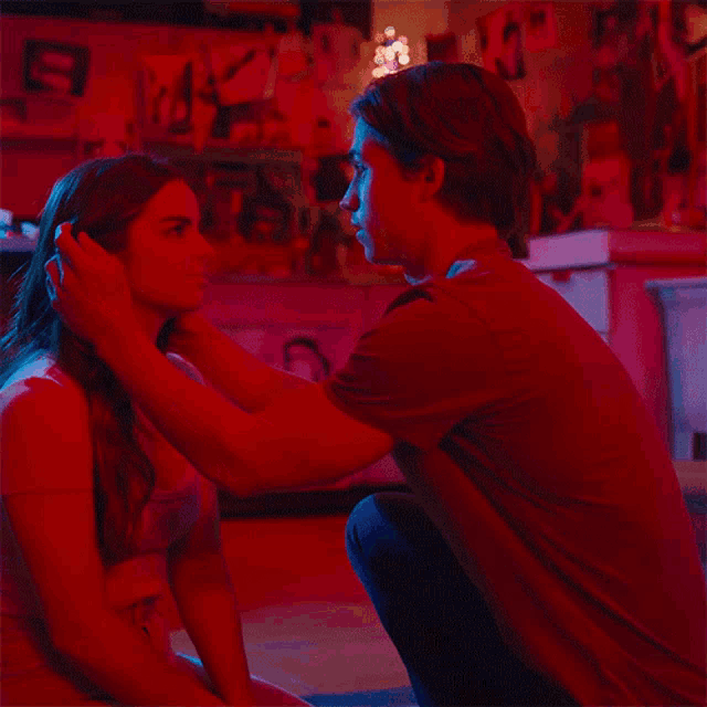 a man in a red shirt is touching a woman 's face in a red room