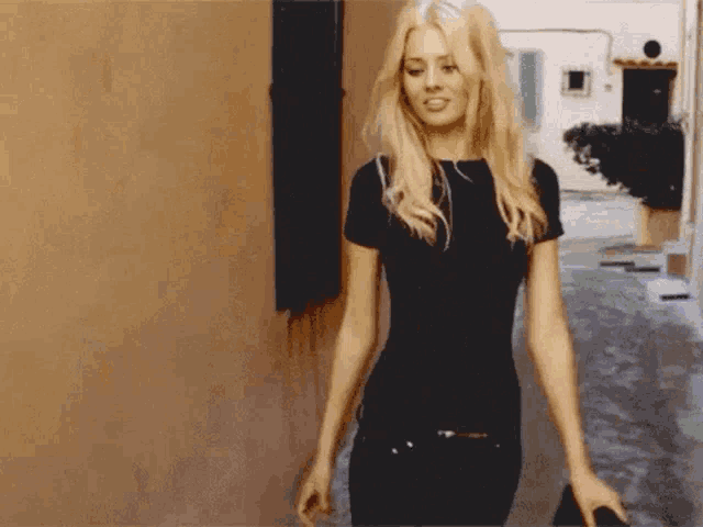 a blonde woman in a black shirt is walking down a sidewalk