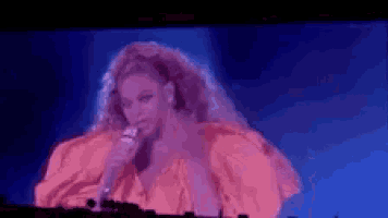 a woman in an orange dress is holding a microphone on a stage .
