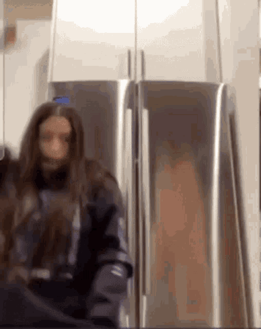 a woman with long hair is standing in front of a refrigerator .
