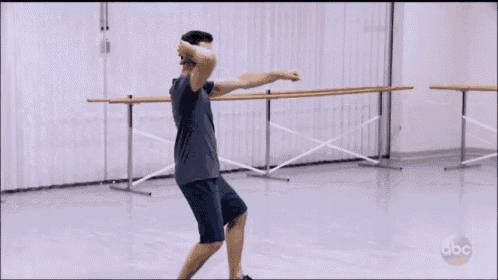 a man in a gray shirt and blue shorts is dancing in a dance studio on abc