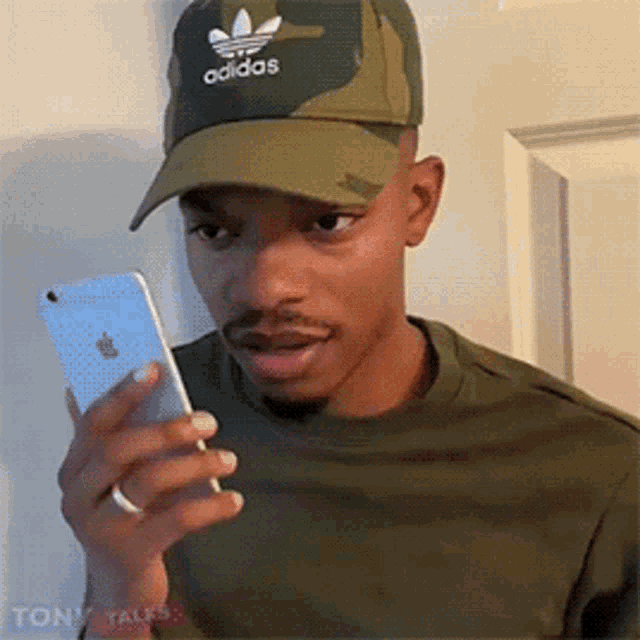 a man wearing an adidas hat is looking at his iphone .