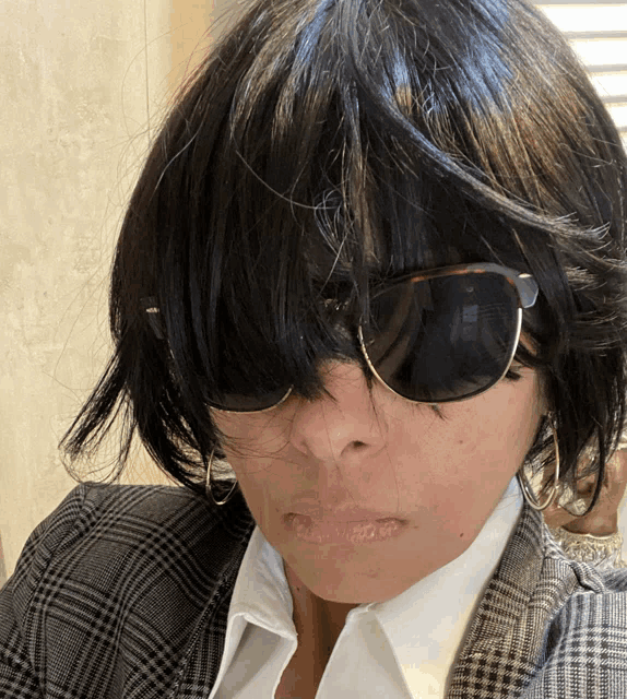a woman wearing sunglasses and a plaid jacket has her hair covering her eyes