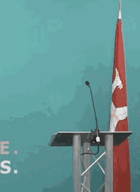 a man in a suit and tie is standing at a podium with a flag behind him .