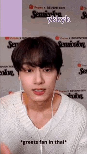 a young man wearing headphones and a white sweater says " greefts fan in thai "