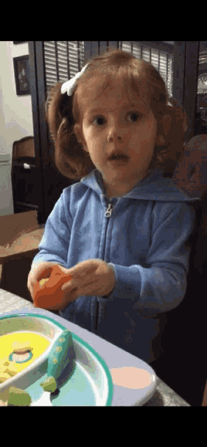 a little girl in a blue jacket holds an orange