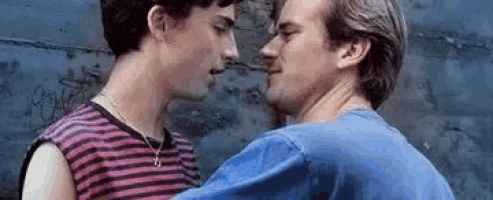 a couple of men are kissing each other in front of a wall .