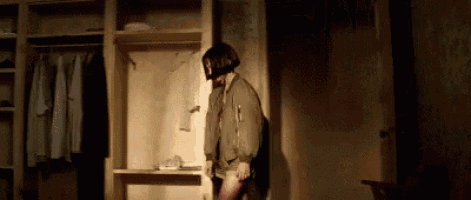a woman in a bomber jacket is standing in a dark room in front of a closet .
