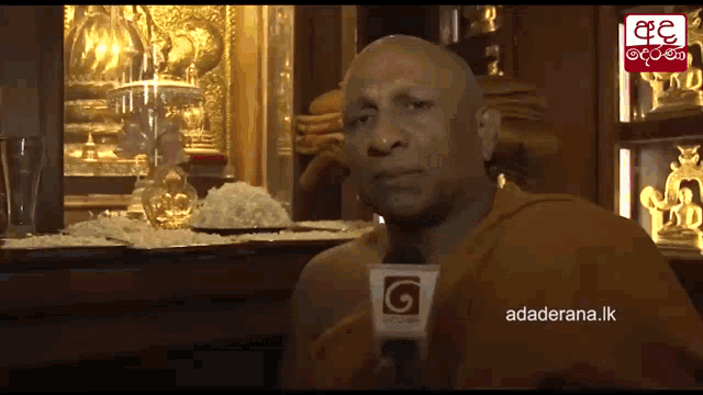 a man in a monk 's robe is talking into a microphone with a g on it