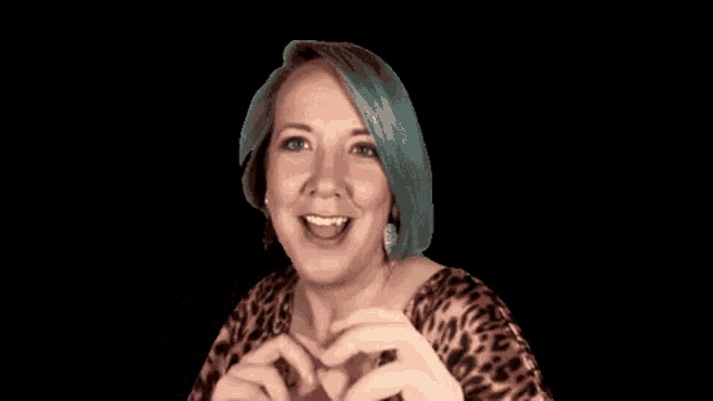 a woman with blue hair is wearing a leopard print shirt and making a funny face with her hands in the air .