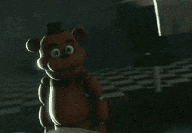 a brown teddy bear is standing in a dark room looking at the camera
