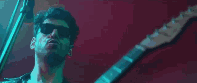 a man in sunglasses is playing a guitar in front of a microphone .