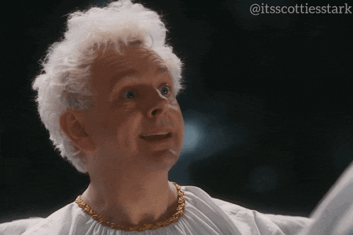 a man with white hair and a gold chain around his neck looks up
