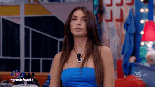 a woman in a blue strapless top is sitting in front of a sign that says grandefratello
