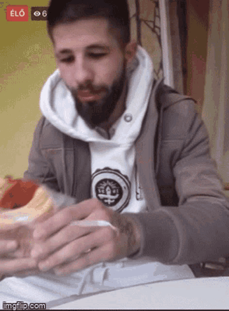 a man with a beard is sitting at a table eating a sandwich with a red button that says elo on it
