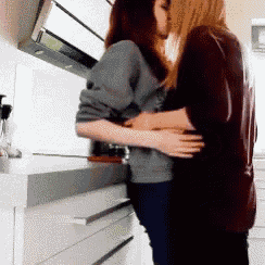two women are kissing in a kitchen and hugging each other