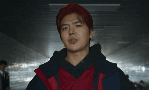 a young man with red hair and a red vest is pointing at the camera