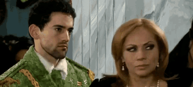 a man and a woman are standing next to each other in a room . the man is wearing a green military uniform .