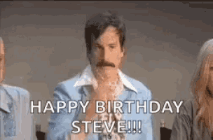 a man with a mustache is sitting in front of a group of people and says `` happy birthday steve ! ''