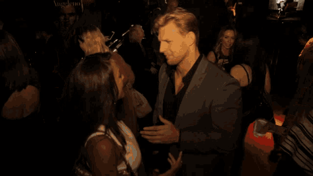 a man in a suit is talking to a woman in a crowded room