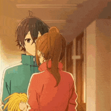 a boy and a girl are kissing in a hallway while holding pom poms .