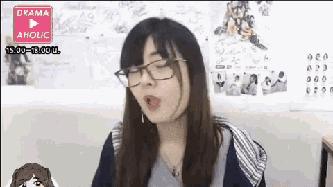 a woman wearing glasses and a necklace is sitting in front of a wall with drawings on it .