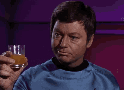 a man in a blue shirt is holding a glass with a yellow liquid in it