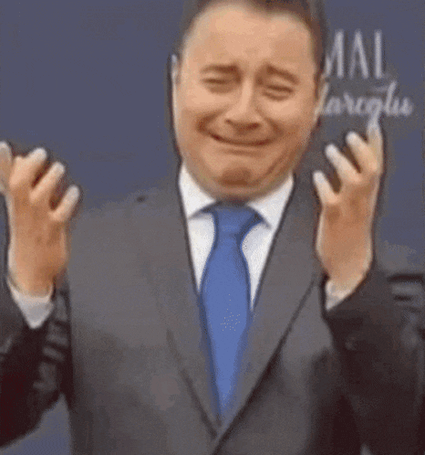 a man in a suit and tie is making a funny face with his hands up .