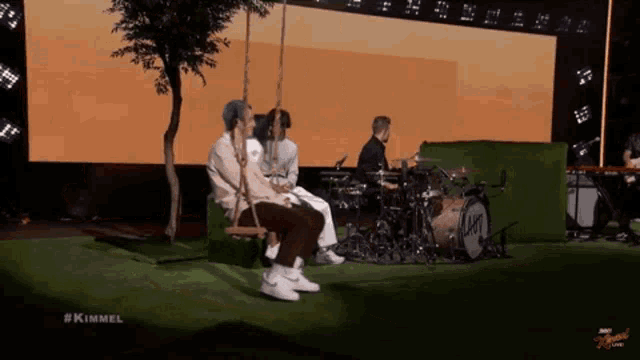a group of people sitting on a swing in front of a drum set that says kimmel on it