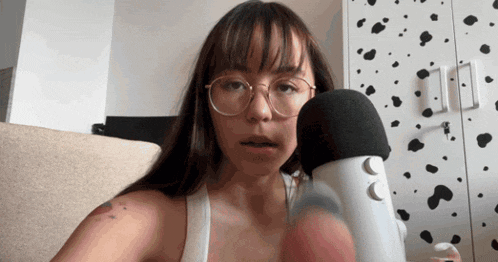 a woman wearing glasses holds a microphone in front of a dalmatian wall