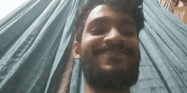 a man with a beard is smiling and looking at the camera while sitting in front of a blue curtain .