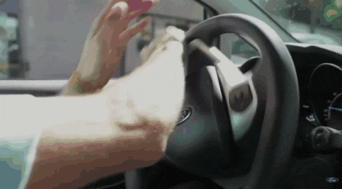 a person 's hand is on the steering wheel of a ford vehicle