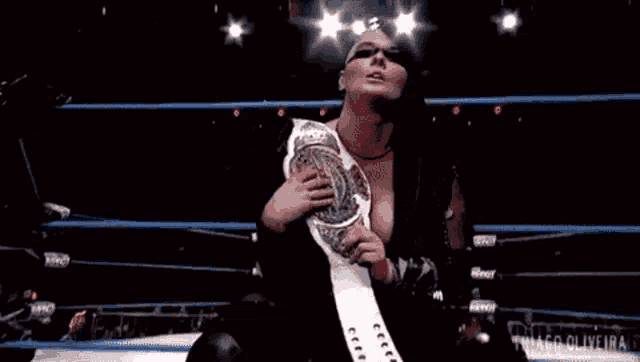 a woman is holding a championship belt in a wrestling ring .