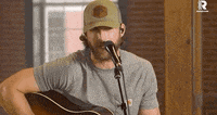 a man with a beard is singing into a microphone while holding a guitar .