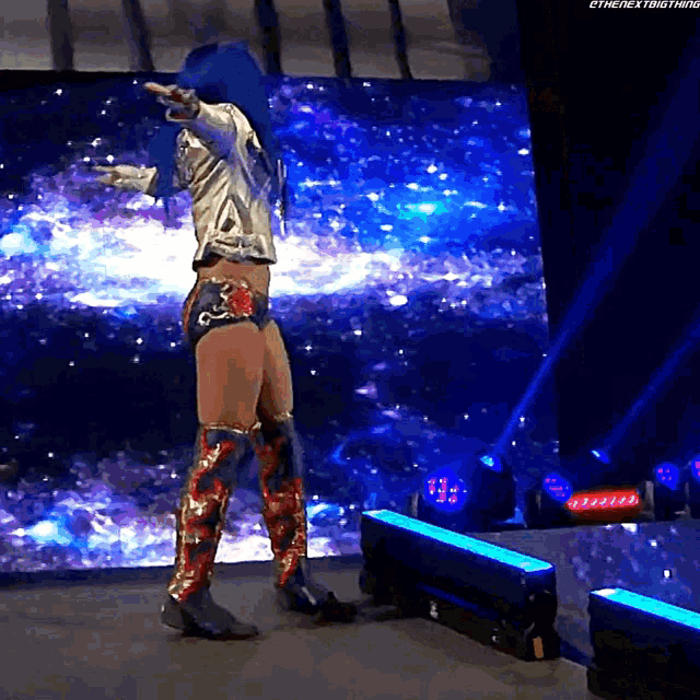 a woman with blue hair is standing on a stage in front of a screen that says the next thing