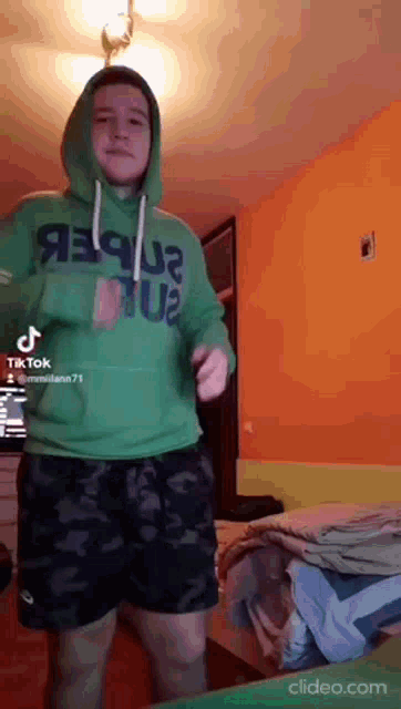 a man in a green hoodie is dancing in a bedroom .