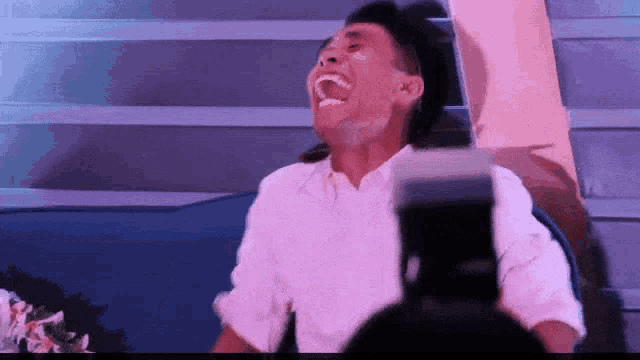 a man in a white shirt is laughing in front of a camera .