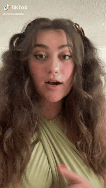 a woman with long curly hair is wearing a green top and making a funny face
