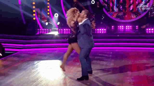 a man in a suit is holding a woman in his arms on a stage with dancing brasil on the screen