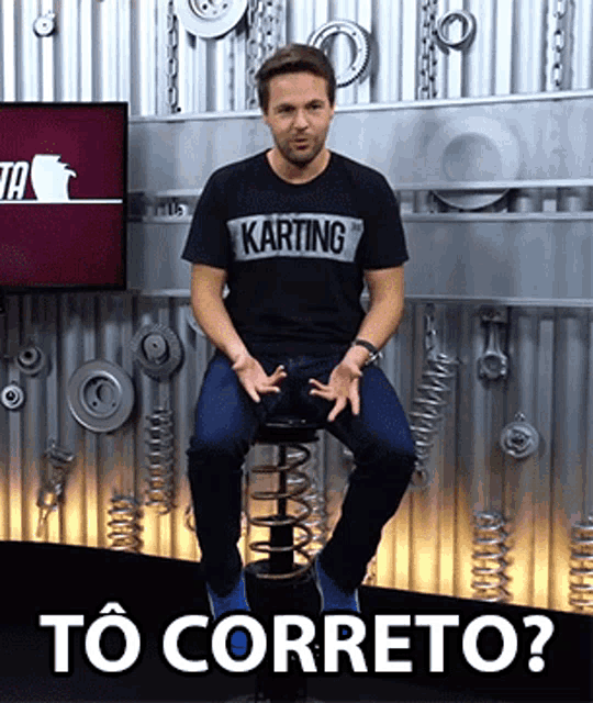a man wearing a karting t-shirt sits on a stool