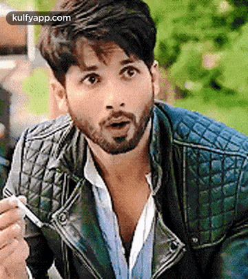 a man with a beard is wearing a leather jacket and holding a cigarette .