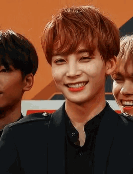 a young man with red hair is smiling while standing next to two other young men .