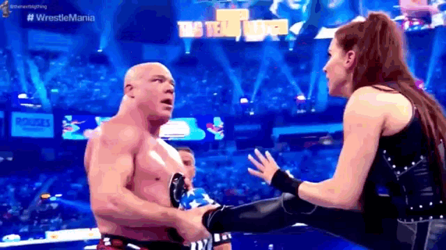 a man and a woman are wrestling in a stadium and the woman is kicking the man 's leg .