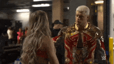 a man and a woman are standing next to each other in a room . the man is wearing a gold and red outfit .